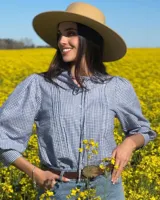Blusa de manga larga con estampado de cuadros vichy en tonos azul y blanco, cuello alto con volados y lazo para anudar, pliegues frontales y cierre con botones nacarados.