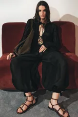 Top de manga larga negro, de tejido de punto semitransparente con efecto fruncido horizontal. Presenta cuello redondo con borde festoneado y cierre frontal con lazos finos.