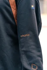 Buzo amarillo de corte holgado con mangas raglán en color azul, detalle de costuras acolchadas en los hombros y bordado de sol en el centro del pecho. Presenta puños y cuello acanalados con rayas azules.