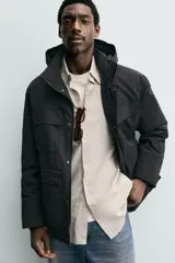 Parka técnica de corte relajado con interior ligeramente acolchado. Presenta cuello subido con capucha ajustable, cierre frontal con cremallera oculta por solapa con botones a presión, y cuatro bolsillos frontales de plastrón con solapa. Incluye cintura ajustable con cordón interior, puños con rib y aberturas laterales con cremallera en el bajo.