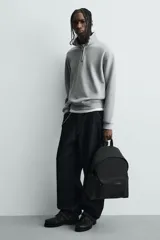 Mochila negra lisa con acabado engomado, compartimento principal con cierre de cremallera, bolsillo interior con cremallera, bolsillo frontal con cremallera, parte posterior acolchada con banda de sujeción para equipaje, asa de mano y dos asas de hombro ajustables y acolchadas.