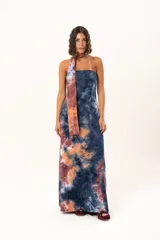 Vestido largo de corte recto y escote strapless, con estampado estilo batik en tonos azul, naranja y bordó. Incluye una bufanda larga integrada al diseño que cae desde el cuello.
