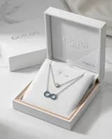 Collar doble de plata 925, compuesto por una cadena superior con dije de punto de luz y una cadena inferior con dije en forma de símbolo de infinito decorado con circonias turquesas.