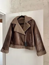 Campera marrón de cuero sintético con interior de piel sintética color beige, cierre cruzado con cremallera y hebilla en el cuello.