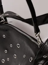 Bolso tipo baguette negro con textura de cuero y múltiples ojales metálicos.