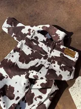 Pantalón vaquero de corte recto con estampado animal print tipo vaca en tonos marrón y blanco, con bolsillos delanteros de tela lisa y aberturas en los tobillos.