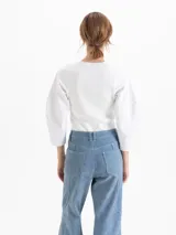 Top de tejido de punto acanalado en color blanco, con cuello redondo y mangas tres cuartos de tela plana con volumen. Presenta un diseño ajustado al cuerpo que contrasta con la estructura de las mangas.