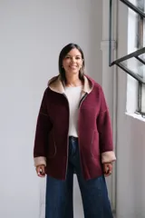 Tapado de paño bordó con interior en color beige, diseño con capucha, cierre frontal y bolsillos laterales. Presenta costuras visibles y puños vueltos que dejan ver el contraste de color.