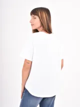 Remera blanca de algodón con cuello redondo y mangas cortas. Presenta un estampado frontal con pinceladas de colores y la frase 'in love we trust'.