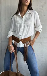 Camisa blanca de corte clásico con cuello camisero, mangas largas y detalle de bordado geométrico en el panel frontal superior. Confeccionada en tela liviana con textura.