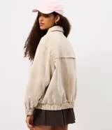 Campera bomber oversized de poliuretano con acabado efecto gamuza en color beige. Presenta cuello camisero, cierre frontal, mangas largas con puños abotonados y ruedo elástico.