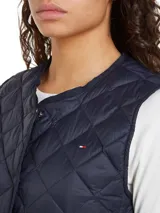 Chaleco azul marino acolchado con relleno de plumón, sin cuello y cierre a presión. Cuenta con el logo de Tommy Hilfiger bordado en el pecho.