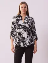 Blusa de gasa estampada en blanco y negro con diseño floral, marca Floral & Ivy. Tiene cuello a la base con escote en V y mangas 3/4 regulables con presilla y botón.