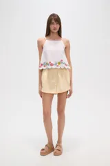 Top de algodón blanco con breteles finos regulables y escote cuadrado. Presenta un diseño holgado con bordado floral multicolor en el ruedo y terminación festoneada.