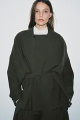 Trench corto de Zara, confeccionado en mezcla de lyocell, color verde militar. Presenta cuello solapa, manga larga con hombro caído y puños con trabilla. Incluye bolsillos delanteros de plastrón, cierre frontal cruzado con botón y cinturón de lazada en el mismo tejido.
