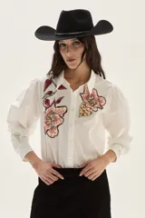 Camisa blanca de algodón con bordados florales en tonos rosados y rojizos en el frente. Presenta mangas largas abullonadas y puños con bordado.