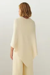 Ruana de tejido de punto industrial en color marrón, confeccionada en lana fina sin teñir. Presenta un diseño con doble ojal que permite mantener la prenda cruzada y cerrada.