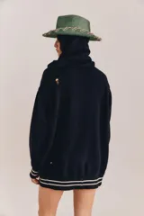 Sweater de punto negro con capucha y cuello en V, de manga larga y diseño holgado. Cuenta con el nombre de la marca bordado en el frente en color blanco, bolsillo estilo canguro, y detalles de rayas blancas en contraste en los puños y el ruedo.