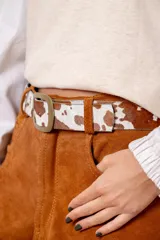 Cinturón de cuero con acabado de pelo sintético estampado con diseño de manchas tipo animal print, con hebilla metálica rectangular en tono bronce envejecido.