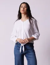 Blusa blanca de algodón marca Dash, con escote en V, abertura con botones, mangas 3/4 regulables con presilla y botón, y terminación de ruedo anudado.