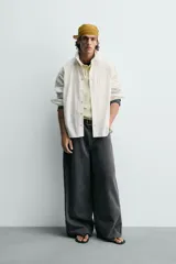 Camisa blanca de algodón con corte relajado, cuello solapa, manga larga con puño abotonado y bolsillo de plastrón en el pecho. Presenta bajo asimétrico con aberturas laterales y cierre frontal de botonadura.