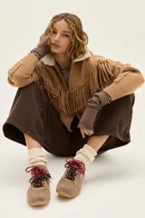 Zapatilla de cuero marrón con paneles de gamuza y cuero liso, suela de goma color caramelo y cordones bicolores en rosa y blanco.