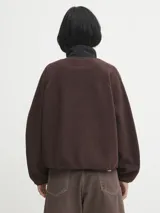 Campera de polar negro con textura de borreguito, cierre frontal con botones a presión y paneles de nylon contrastantes en el pecho. Cuenta con bolsillos laterales con cierre y el logo de la marca aplicado en el pecho.