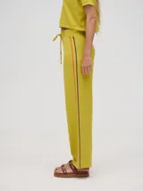 Pantalón de punto color verde oliva, confeccionado en algodón, con corte holgado, pierna ancha y tiro alto. Cuenta con pretina elástica con cordón de ajuste y una línea lateral a contratono en color naranja.