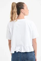 Remera blanca de manga corta y corte holgado, confeccionada en algodón orgánico, con detalle de volado fruncido en el ruedo.