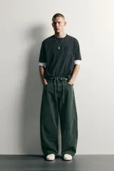 Pantalón barrel fit de mezclilla color verde militar, con efecto lavado, cinco bolsillos, cierre frontal con cremallera y botón, y detalle de pinzas en las rodillas.