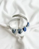 Brazalete rígido abierto de metal plateado con tres piedras de lapislázuli incrustadas.