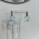 Aros de acero quirúrgico hipoalergénico con dije de acrílico blanco con diseño de caracol en azul.