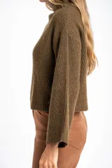 Polera de lana oversize color beige melange, con cuello alto, mangas largas acampanadas y diseño de tejido acanalado con tramas direccionales.