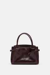 Bolso tipo mini city confeccionado en piel con acabado texturizado. Presenta doble asa de mano, detalle de tiras laterales y herrajes metálicos dorados. Cuenta con compartimento principal, bolsillos exteriores y bolsillo interior.