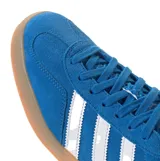 Championes Adidas Gazelle Indoor de gamuza azul con las icónicas tres rayas laterales en blanco. Presenta una suela de caucho color caramelo, talón blanco y detalles dorados con el nombre del modelo en el lateral.
