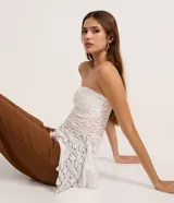 Blusa sin breteles de encaje blanco, con escote recto, diseño ajustado y dobladillo asimétrico con puntas diferenciadas.