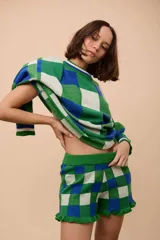 Short tejido en algodón con diseño a cuadros en verde, blanco y azul. Tiene cintura elastizada y volados en el ruedo.