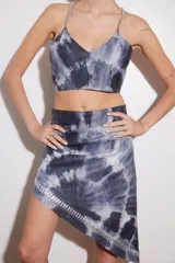 Vestido corto de cuero ovino con diseño batik en tonos de azul y blanco. Presenta tiras de cuero plateado en el escote y ruedo con detalle de ojales metálicos.