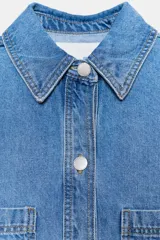 Sobrecamisa de denim celeste, de corte holgado, con cuello solapa, manga larga y bolsillos de plastrón en el delantero. Cierre frontal con botones.