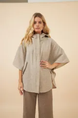 Capa amplia con capucha, confeccionada en lana fina sin teñir. Presenta cierre frontal, bolsillos delanteros y botones laterales que permiten ajustar la forma de las mangas.