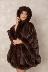 Capa de piel sintética en color negro, con diseño holgado, capucha integrada y bordes con textura de pelo largo.