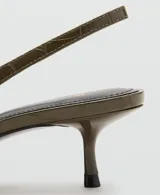 Zapatos destalonados de tacón fino y punta afilada, en color verde militar con textura efecto cocodrilo y detalle de media esfera dorada en la punta.