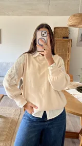 Sweater de punto color natural con cuello polo y mangas largas abullonadas. Presenta detalles bordados con lentejuelas plateadas en los hombros y parte superior de las mangas.