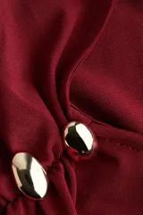 Vestido midi de punto color rojo oscuro (vino/burdeos) con diseño asimétrico de un solo hombro, frunces laterales y detalle de botones dorados en el tirante.