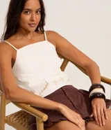 Blusa confeccionada en sarga de algodón, de color blanco, con escote cuadrado y tirantes finos. Presenta un detalle bordado en la parte inferior con motivos botánicos y la palabra ciao.