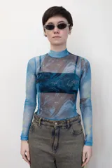Remera traslúcida de cuello alto y mangas largas, con estampado abstracto en tonos celeste, azul y amarillo.