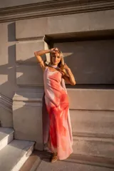 Vestido largo de satén con estampado degradado en tonos rosado, naranja y fucsia. Presenta escote en V, tirantes finos y un pañuelo integrado al cuello.