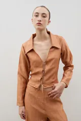 Camisa de manga larga con cuello solapa y cierre frontal mediante lazos para anudar. Presenta una textura arrugada en toda la prenda.