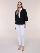 Blusa negra de calce suelto y caída ligera con sutil textura, cuello camisero blanco, escote en V con pechera en contraste y mangas tres cuartos abullonadas con puños elásticos.