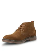 Botas tipo chukka Hush Puppies modelo New Safari, confeccionadas en descarne color marrón tostado. Presentan cordones al tono, costuras reforzadas en la suela y detalle de etiqueta con franjas en el talón.